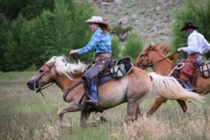 CM Ranch - Two riders galloping on horseback.