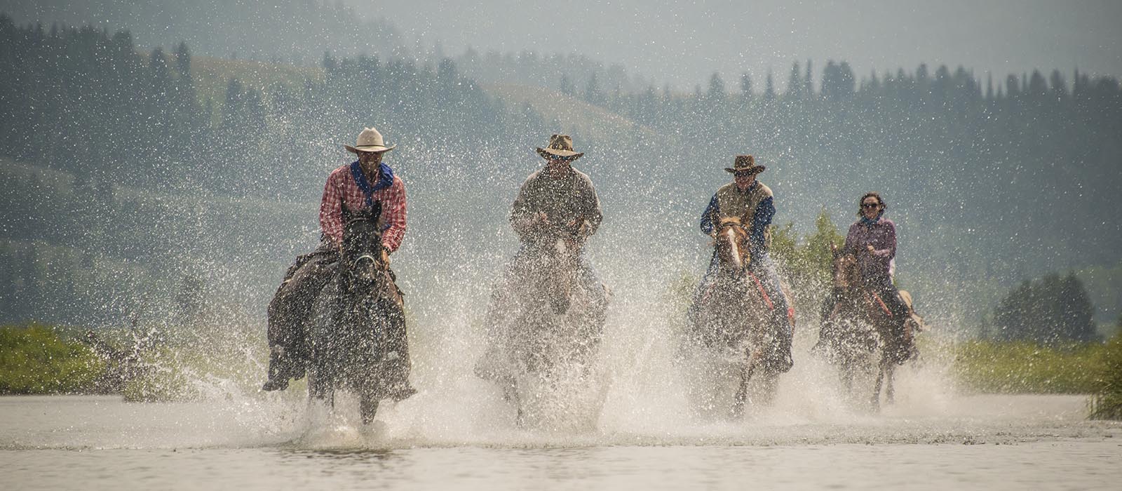 Horseback riders galloping through a river.