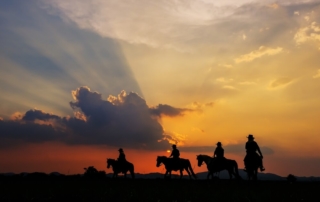 Photo of a group of people riding horses at sunset: corporate retreat ideas